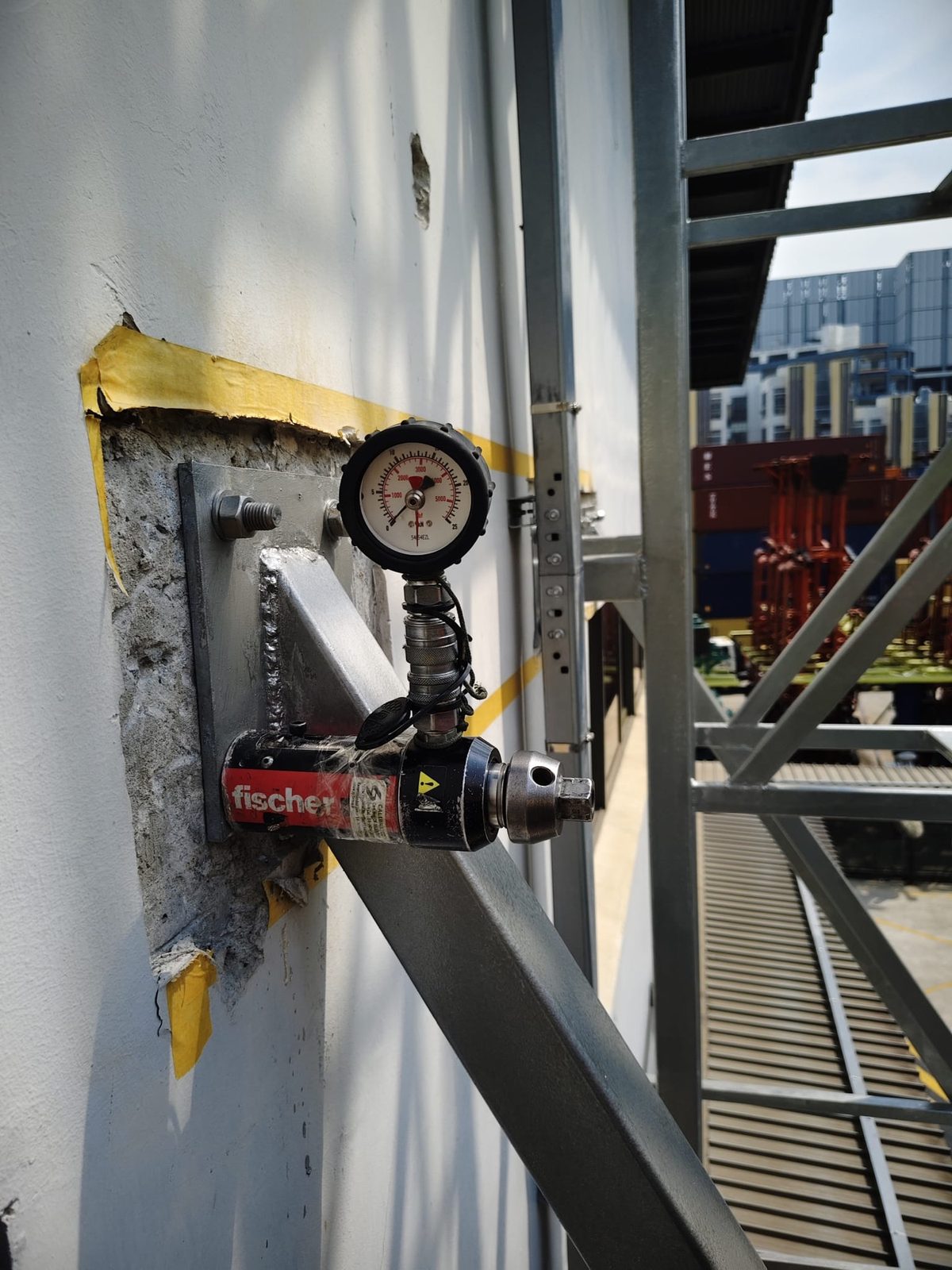 On-site anchor pull-out test on a Fischer chemical anchor with a hydraulic load gauge and reaction frame at the Buroh Street installation