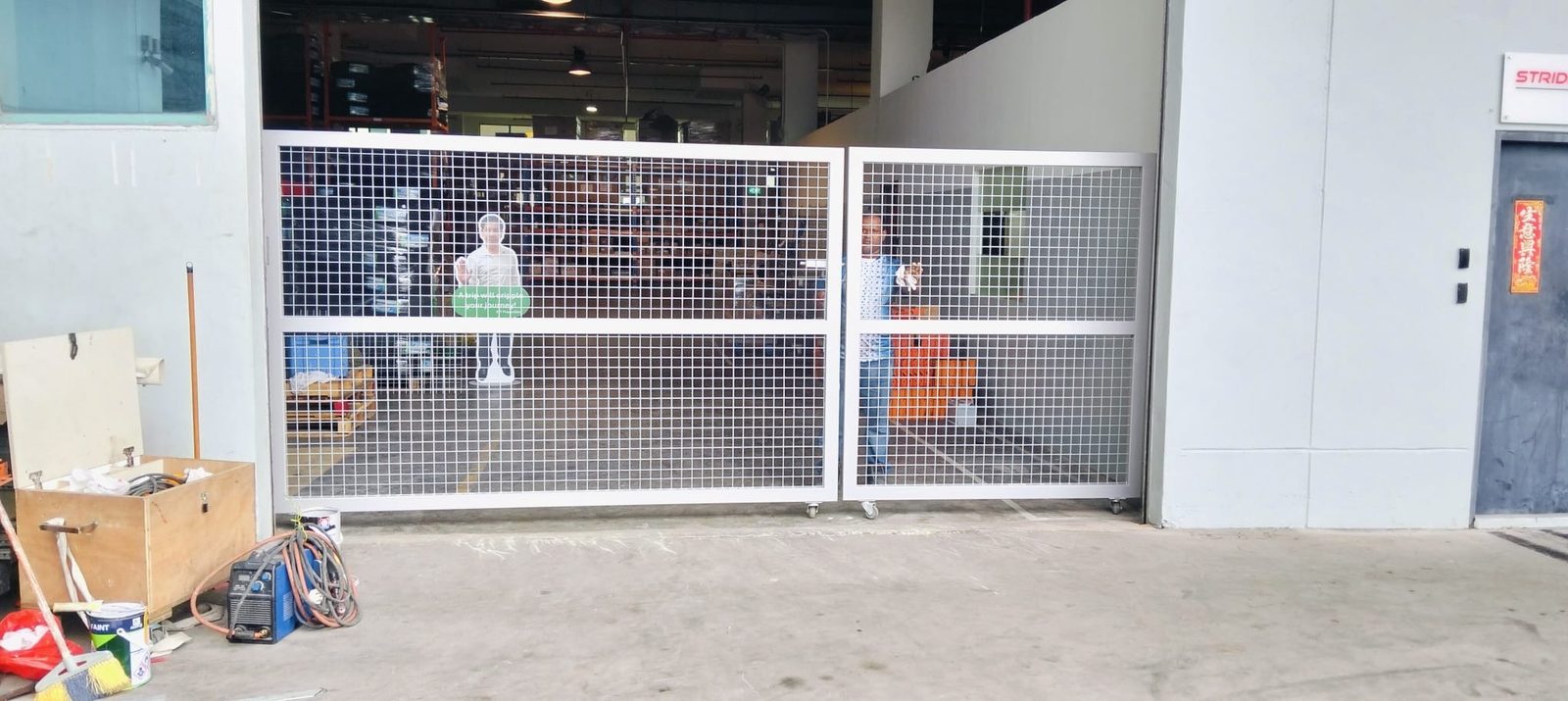 Finished metal gate at Strides Premier — wide front view of the installed mesh-panel gate across the warehouse opening